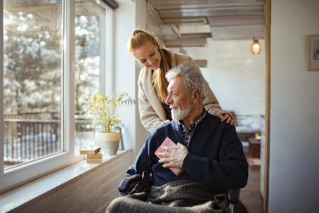 A caretaker looking after an elderly man in a wheelchair at a nursing home during winter